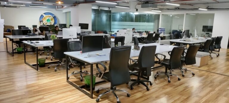 Modern collaborative workspace with wooden tables, pendant lighting, and plants creating a warm office environment